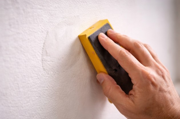 Sanding a patched wall area to achieve a smooth finish
