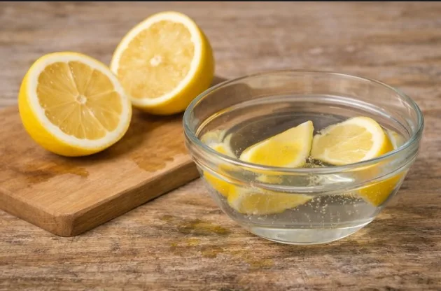 Microwave-safe glass bowl filled with water and lemon slices beside a cut lemon