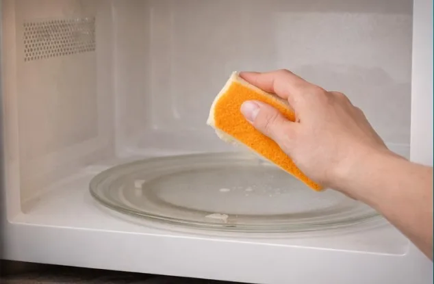 Hand wiping the cool white microwave interior with a soft nonabrasive sponge