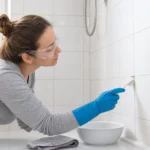 Person wearing gloves and protective goggles cleaning a small bathroom grout spot