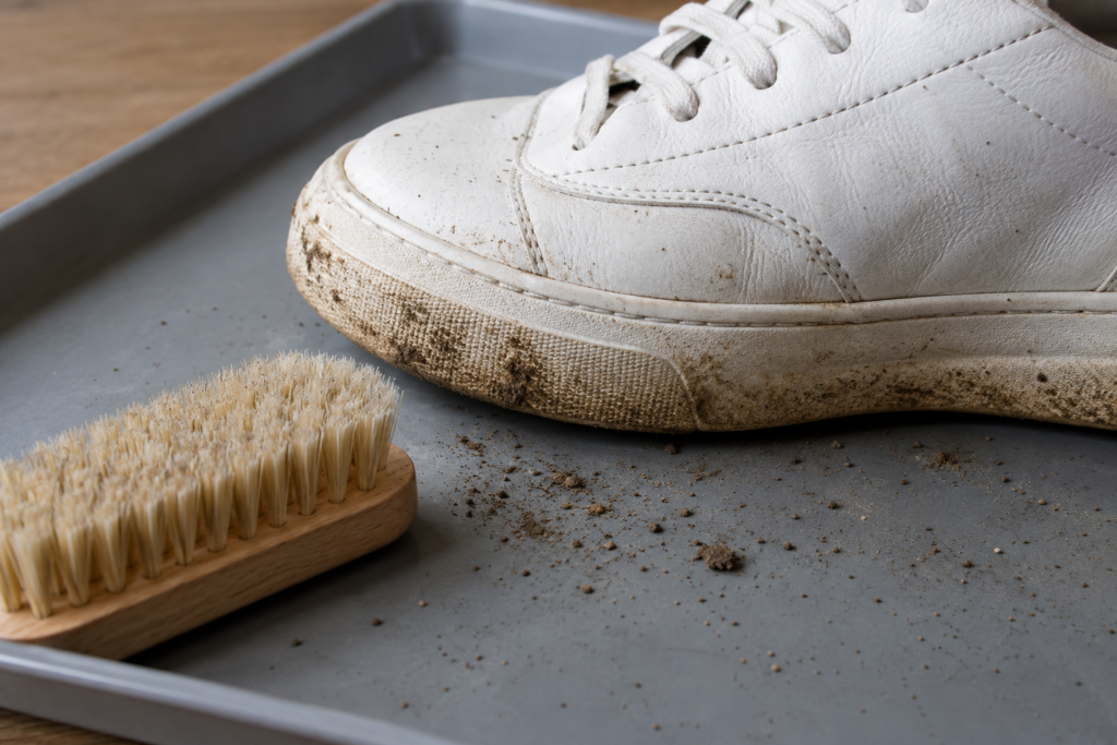 Dry dirt on a white sneaker beside a soft brush