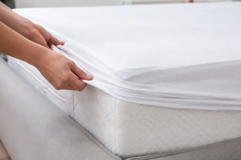 Hands fitting a white mattress protector over a clean mattress