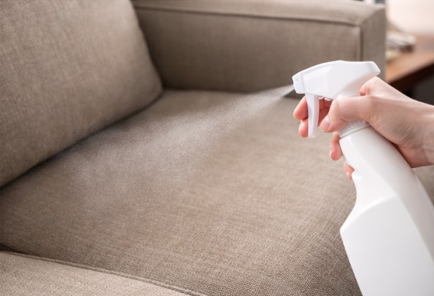 Hand testing a fine fabric-safe mist on a beige upholstered sofa cushion